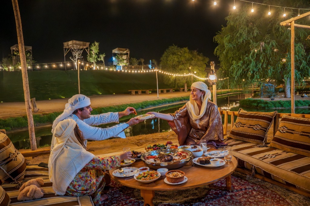 A couple sharing dinner by the lake at night, under strings of lights